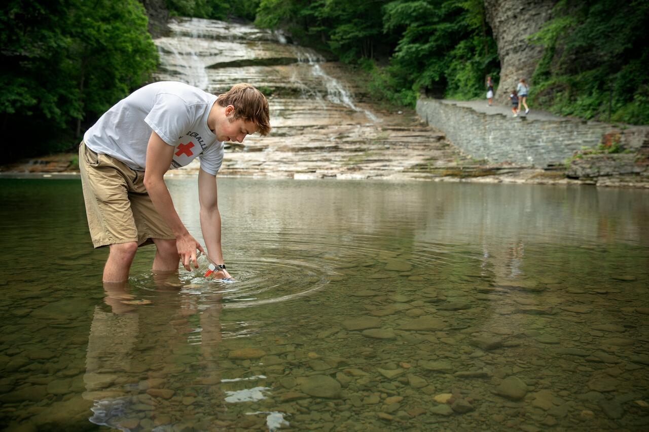 Nate Barott '20, one of five undergraduates on associate professor Ruth Richardson's research team, collects a water sample in June at Buttermilk Falls State Park in Ithaca.
